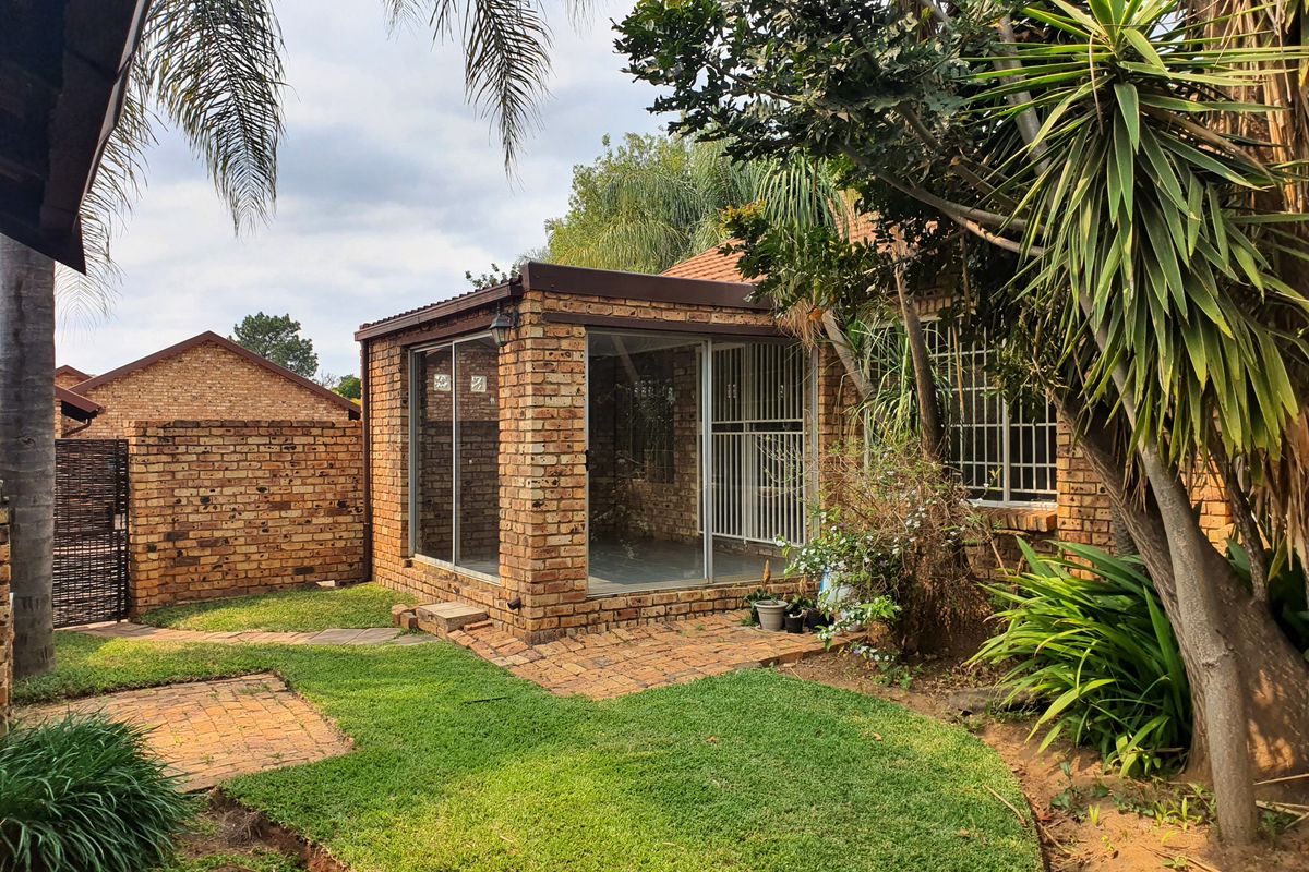 Rear view of the townhouse featuring an enclosed brick patio with sliding glass doors, set within a private garden with established landscaping.