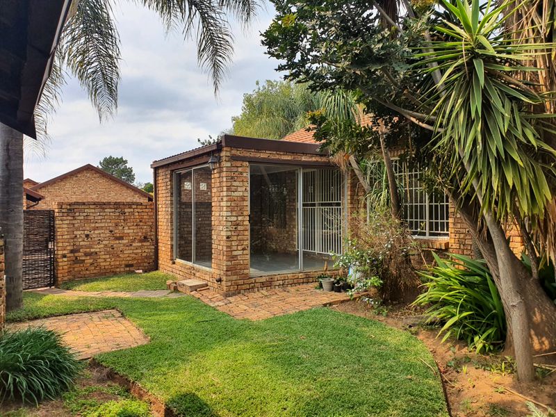 Rear view of the townhouse featuring an enclosed brick patio with sliding glass doors, set within a private garden with established landscaping.