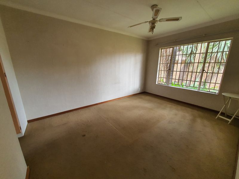 An empty bedroom featuring carpet flooring, a ceiling fan, and security bars on the window, offering a blank canvas for renovation.