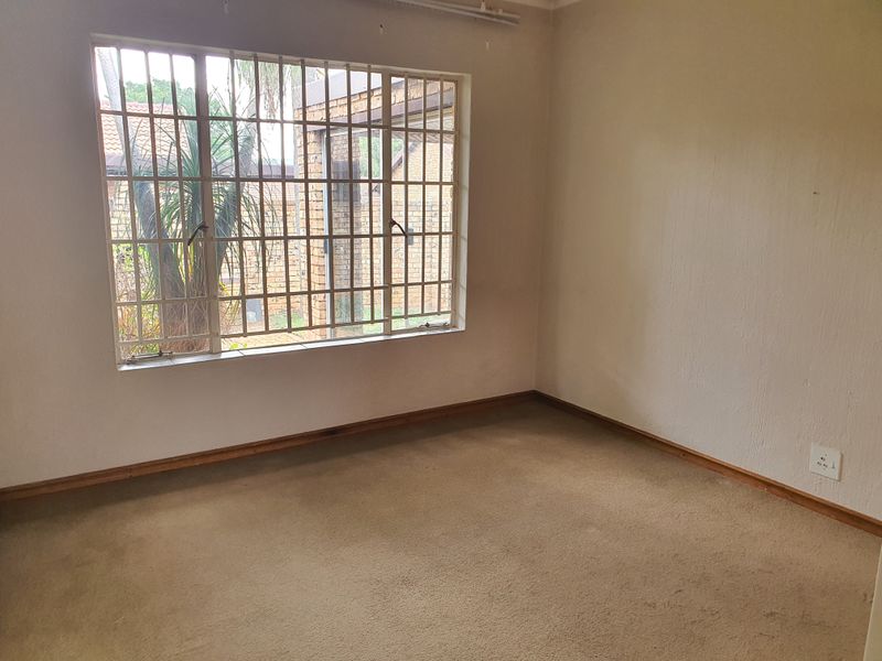 An empty bedroom featuring carpet flooring and a window fitted with security bars, offering a blank canvas for potential updates.