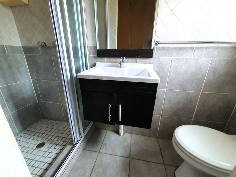 A functional bathroom featuring a shower enclosure, wall-mounted vanity with basin, and a standard toilet, finished with neutral wall and floor tiling.