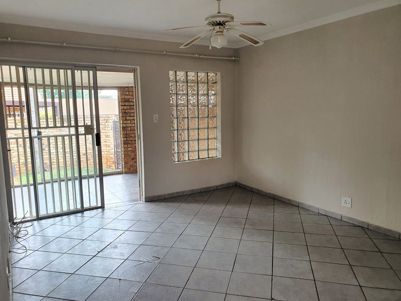 An empty living area featuring tiled floors, a ceiling fan, and a glass block window, with direct access to an outdoor patio area.