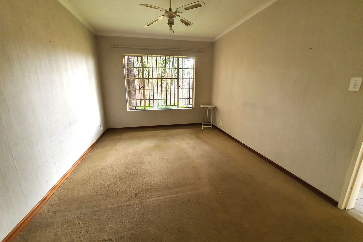 An empty bedroom featuring a ceiling fan, security bars on the window, and carpet flooring, offering a blank canvas for renovation.