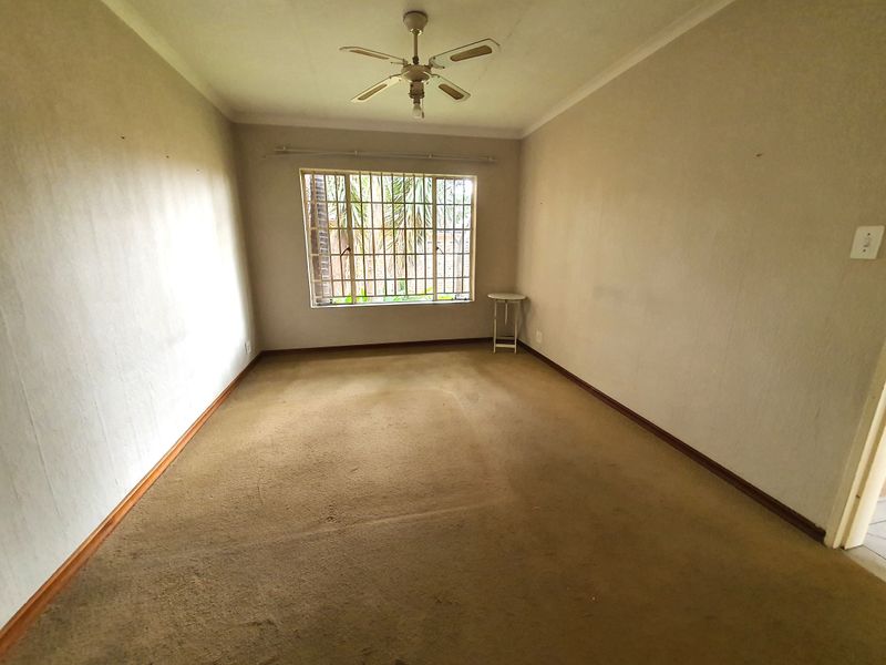 An empty bedroom featuring a ceiling fan, security bars on the window, and carpet flooring, offering a blank canvas for renovation.