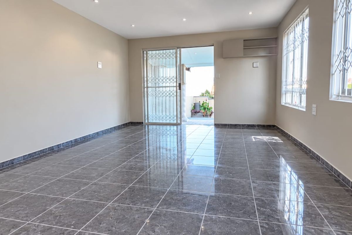A bright, empty living room featuring polished grey tiled flooring, recessed lighting, and direct access to an outdoor patio through a sliding glass door.