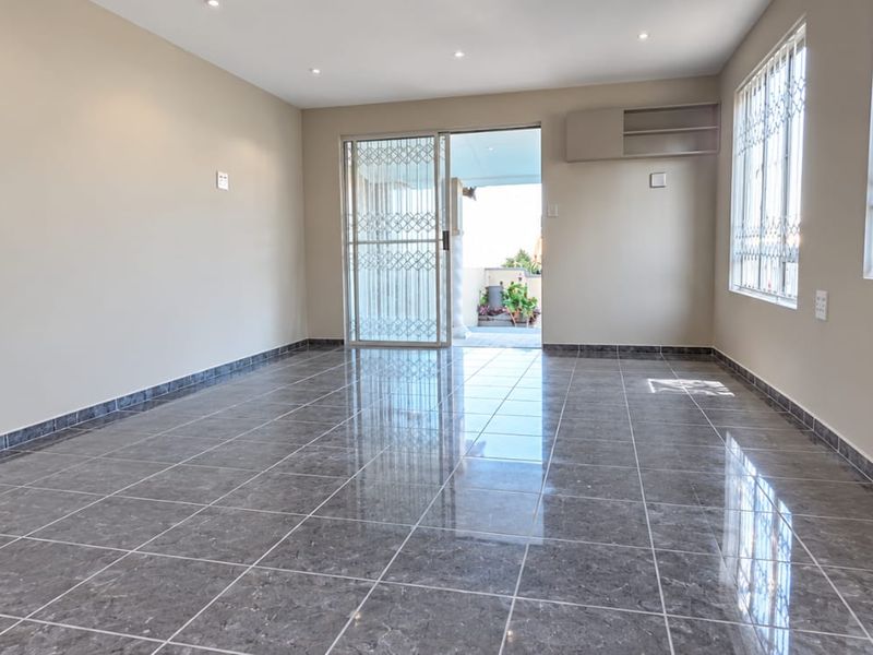 A bright, empty living room featuring polished grey tiled flooring, recessed lighting, and direct access to an outdoor patio through a sliding glass door.