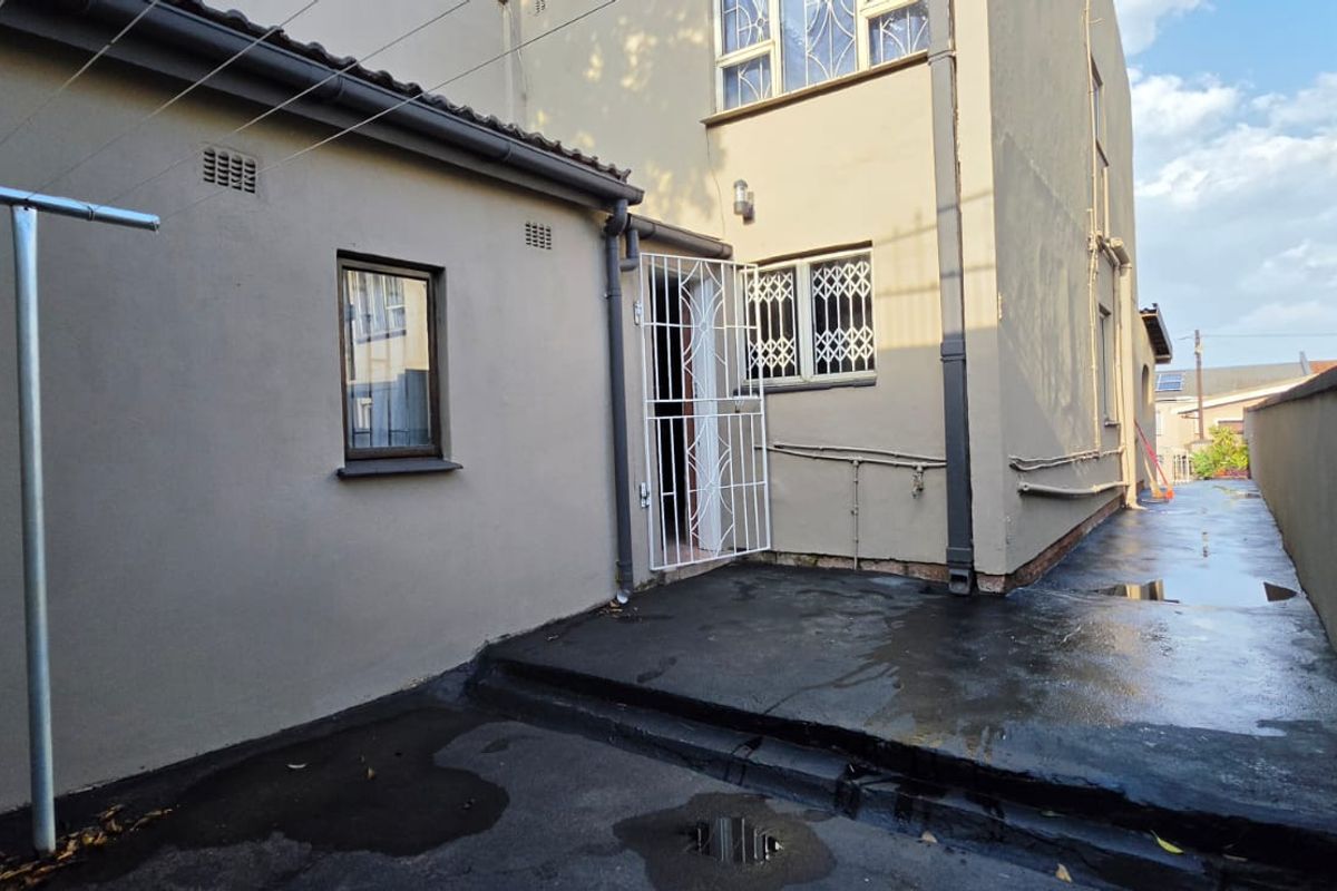 Rear exterior view of the property featuring a paved courtyard area, security gates, and external drainage infrastructure.