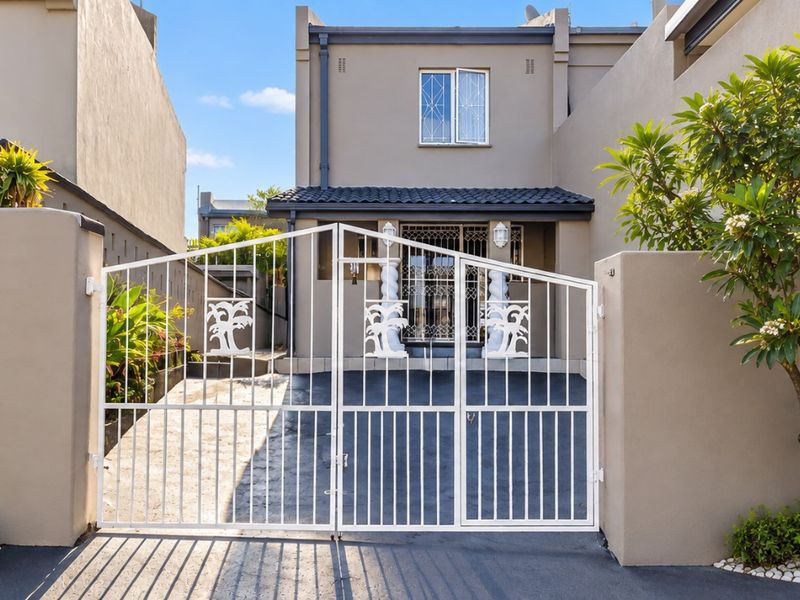 Front elevation of a residential property featuring a secure metal gate, paved driveway, and well-maintained boundary walls.