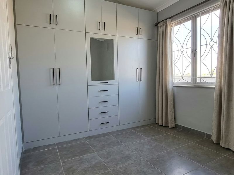 A clean, empty bedroom featuring neutral tiled flooring and extensive built-in cabinetry with integrated drawers and a central mirror panel.