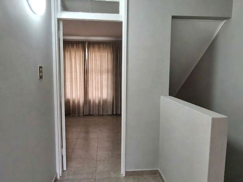 A neutral-toned hallway featuring tiled flooring and a staircase balustrade, leading into an adjacent room with natural light.