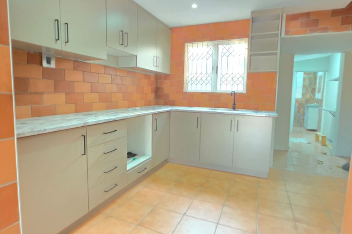 A functional kitchen featuring neutral cabinetry, marble-effect countertops, and distinctive orange tiled walls, offering a blank canvas for modern updates.