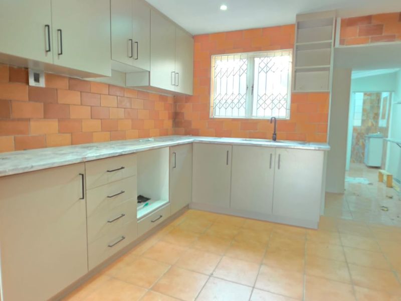A functional kitchen featuring neutral cabinetry, marble-effect countertops, and distinctive orange tiled walls, offering a blank canvas for modern updates.