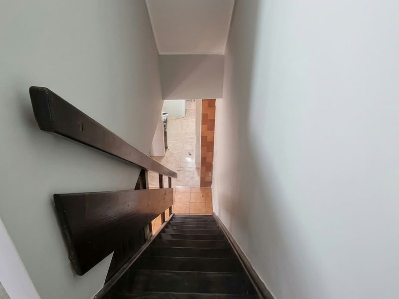 A view looking down a staircase with a wooden handrail, leading to a tiled lower level area.