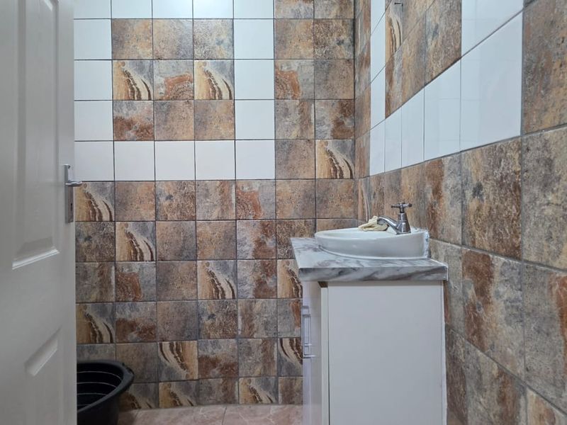 A compact bathroom featuring a vessel sink on a vanity cabinet with decorative stone-look wall tiling.
