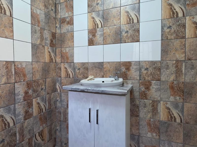 A compact bathroom featuring a modern vessel sink vanity unit and decorative patterned ceramic wall tiling.