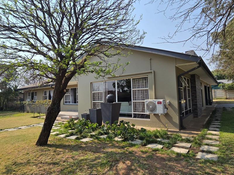 Rear view of the house featuring a landscaped garden, paved walkway, stone cladding accents, and an exterior air conditioning unit.