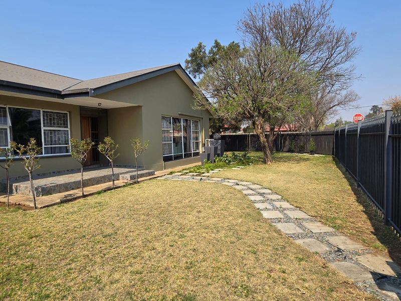 A well-maintained rear garden featuring a stone paver pathway, a tiled patio area, and secure metal perimeter fencing.
