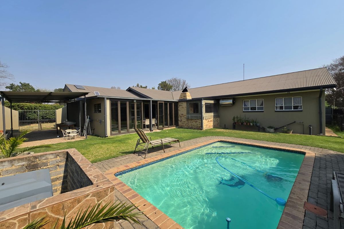 Rear exterior view featuring a swimming pool, paved surround, covered patio area, and a built-in brick braai against the house facade.