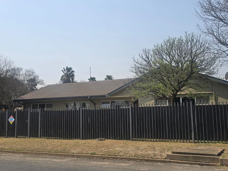 Front view of a single-story house featuring a corrugated metal roof and secure perimeter fencing with window security bars.