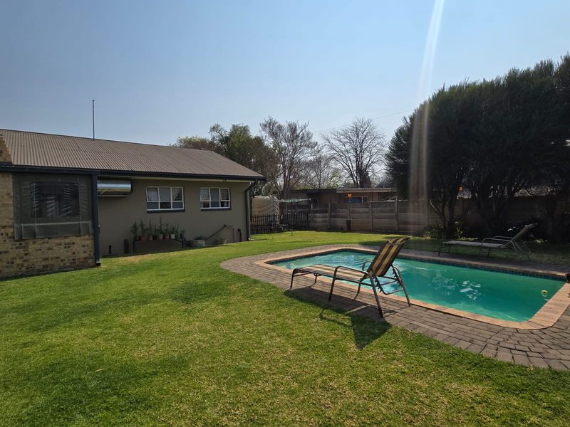 A backyard area featuring a swimming pool with brick coping, a well-maintained lawn, and a rear view of the house with a metal roof.