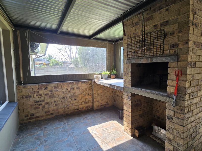 Covered patio area featuring a built-in brick braai, tiled flooring, and roll-up canvas blinds, providing a functional outdoor entertainment space.