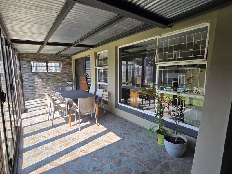 A covered patio area featuring a corrugated metal roof, stone-clad feature wall, and tiled flooring, providing a functional outdoor entertainment space.