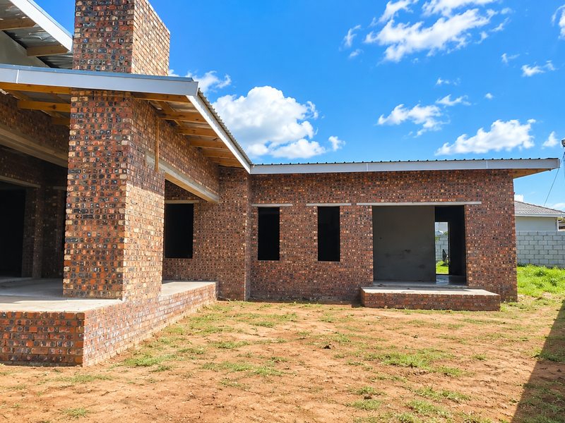 Rear view of a residential property under construction, featuring face brick walls, exposed roof structure, and an unfinished garden area.