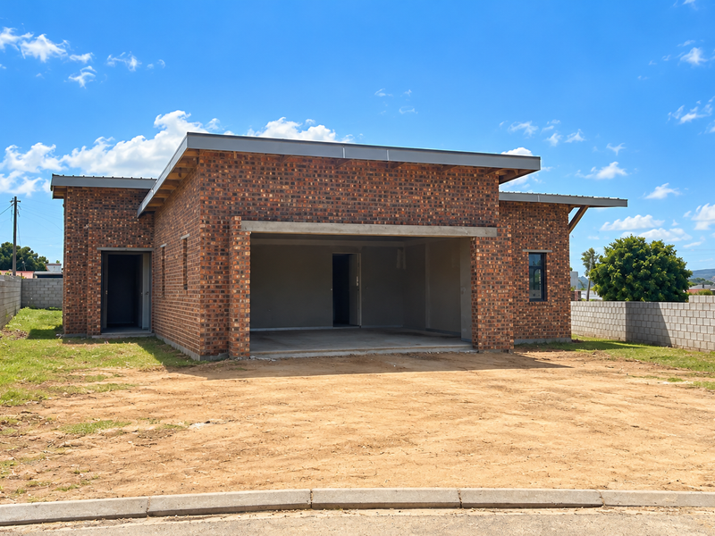 A newly constructed face brick house featuring a flat roof design, double garage, and perimeter boundary walls on a spacious, unlandscaped plot.