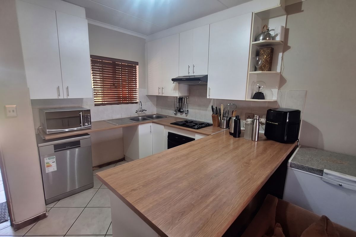 A functional kitchen featuring white cabinetry, wood-look laminate countertops, a gas hob with extractor, and tiled flooring with direct access to the exterior.