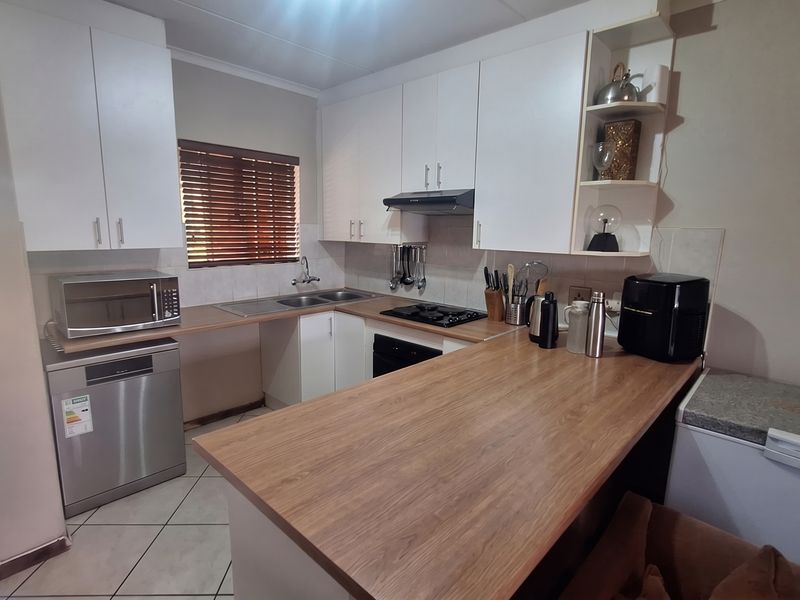 A functional kitchen featuring white cabinetry, wood-look laminate countertops, a gas hob with extractor, and tiled flooring with direct access to the exterior.