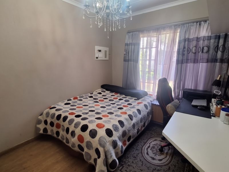 A functional bedroom featuring laminate flooring, a built-in desk area, and a wall-mounted electrical distribution board.