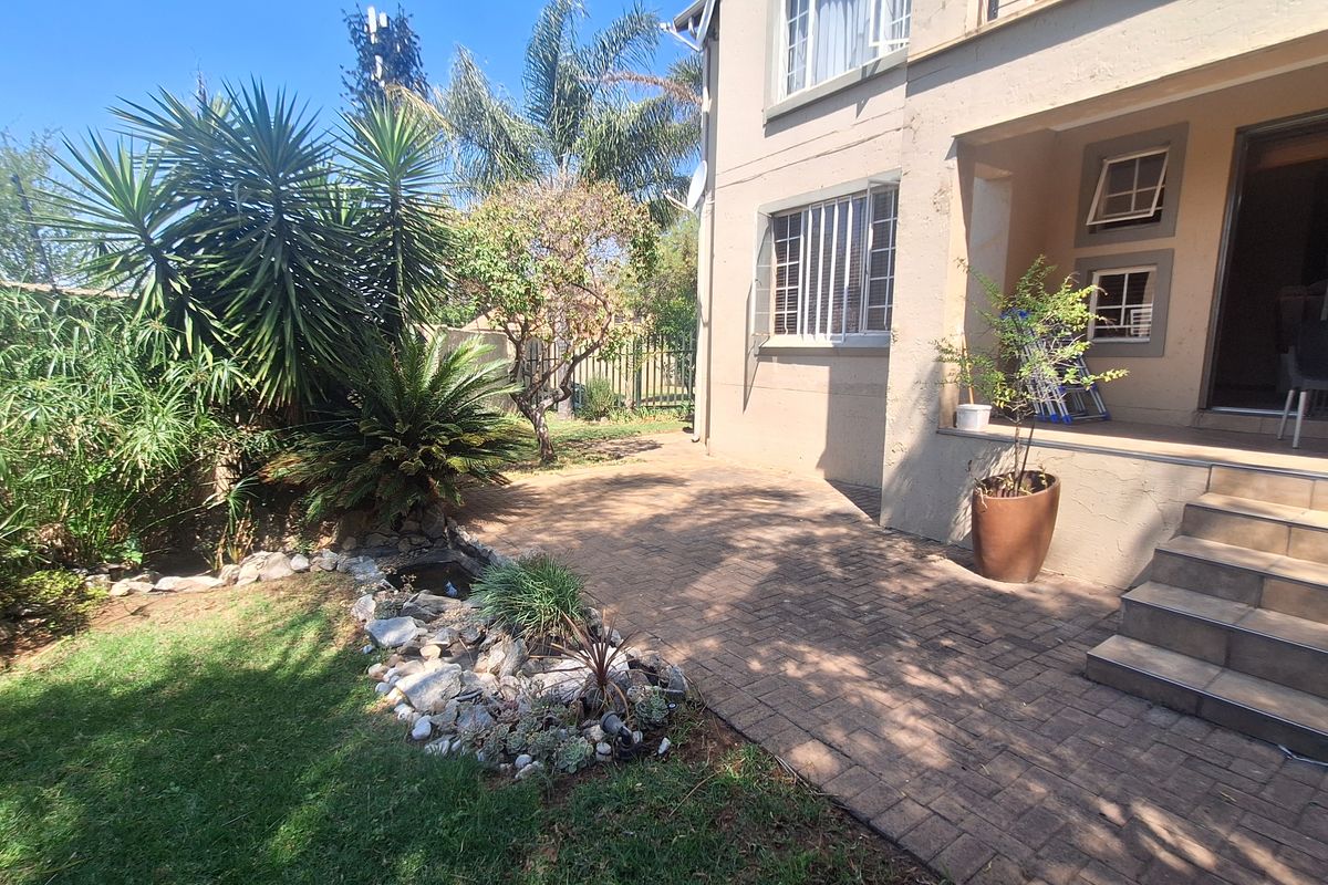 A rear exterior view of the apartment featuring a paved patio area, landscaped garden, and direct access to the building via concrete stairs.