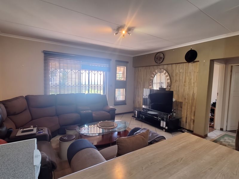 Open plan living area featuring tiled flooring, a wood panel feature wall, and large windows with venetian blinds and security gates.