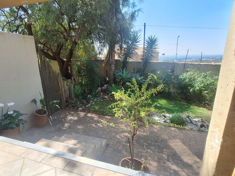 A private garden area featuring a paved patio, established trees, and a boundary wall with views of the surrounding landscape.