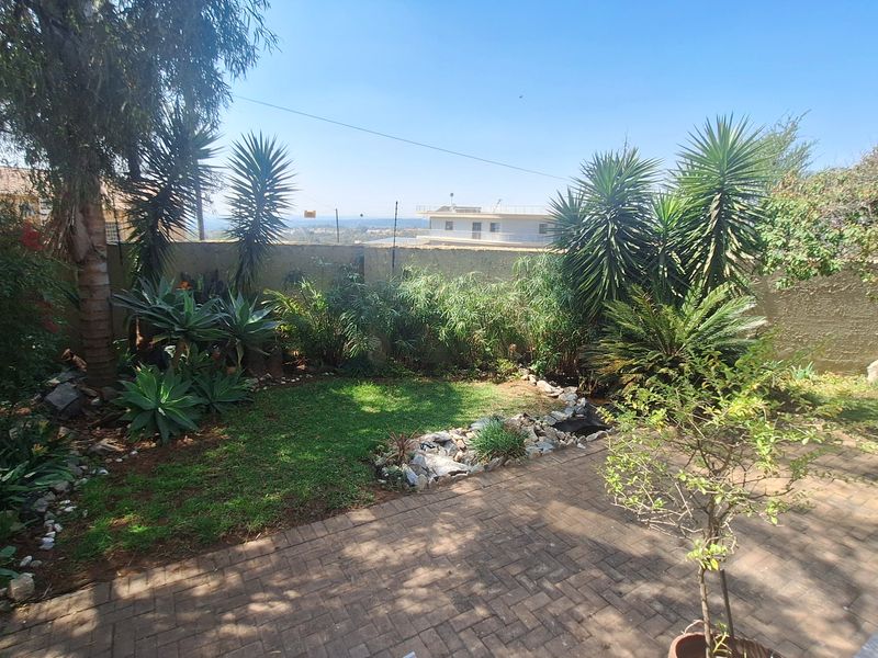 A well-maintained private garden featuring a paved patio area, established landscaping, and a perimeter boundary wall with distant views.