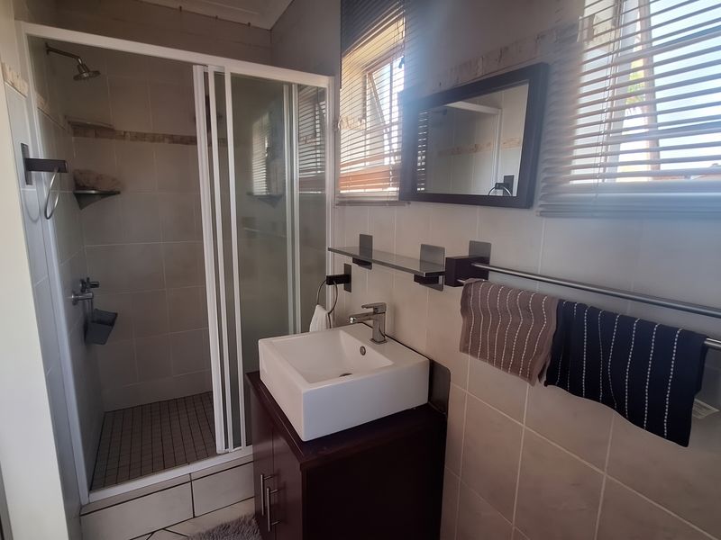 A functional bathroom featuring a shower enclosure, a modern vanity basin with cabinet, and tiled finishes throughout.
