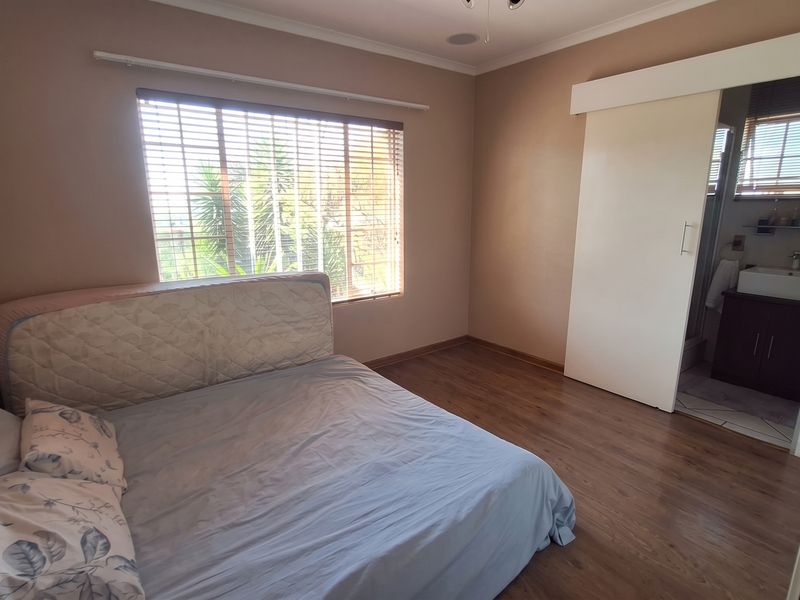 A bedroom featuring laminate flooring, venetian blinds, and a sliding door providing direct access to an en-suite bathroom.