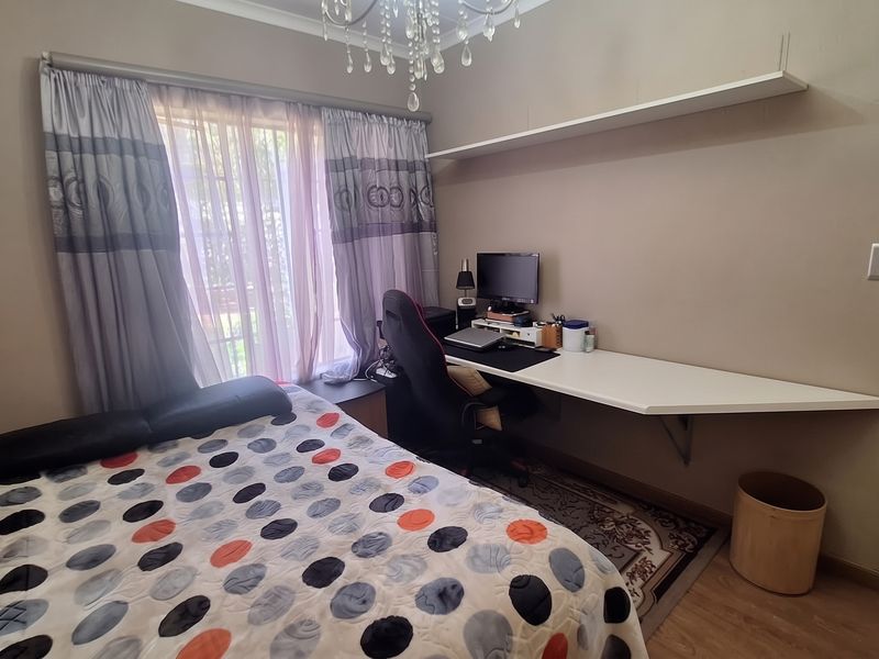A functional bedroom featuring laminate flooring, a built-in desk workspace, and a floating shelf, offering a practical layout for study or rest.