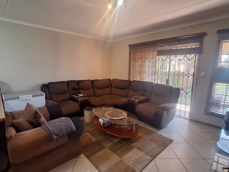 Open plan living area featuring tiled flooring, large sliding glass doors with security gate, and venetian blinds, providing access to the outdoor space.