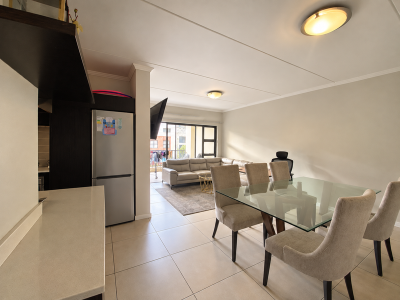 An open-plan living and dining area featuring tiled floors, neutral walls, and a modern kitchen layout with stone countertops and direct balcony access.