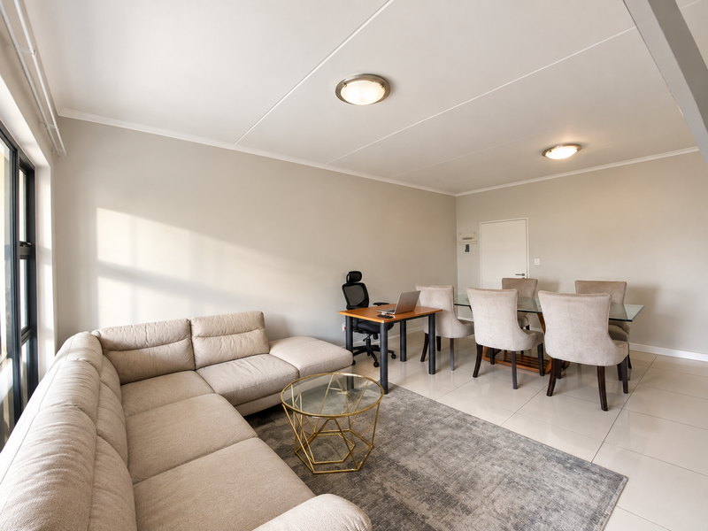Spacious open-plan living and dining area featuring large windows, neutral tiled flooring, and modern flush-mount ceiling lighting.