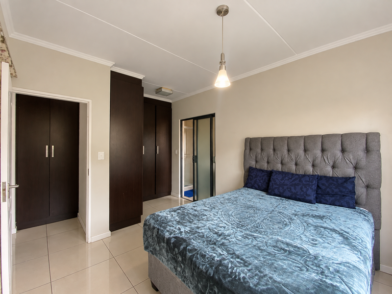 A well-maintained bedroom featuring dark wood built-in cupboards, neutral tiled flooring, and an en-suite bathroom access via a sliding door.