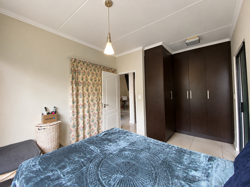 A well-maintained bedroom featuring dark wood built-in cupboards, tiled flooring, and a central pendant light fixture.