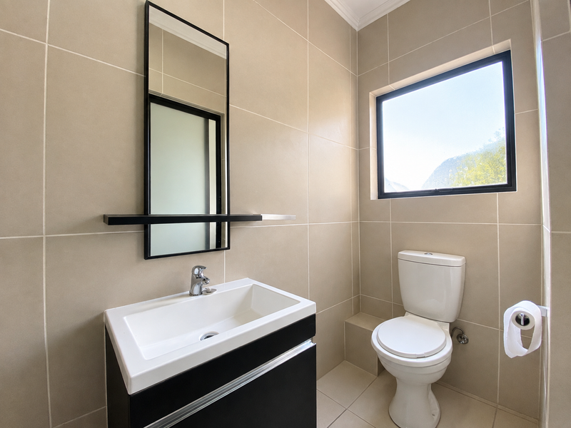 A modern, well-maintained bathroom featuring neutral wall tiles, a sleek vanity with a basin, and a toilet.