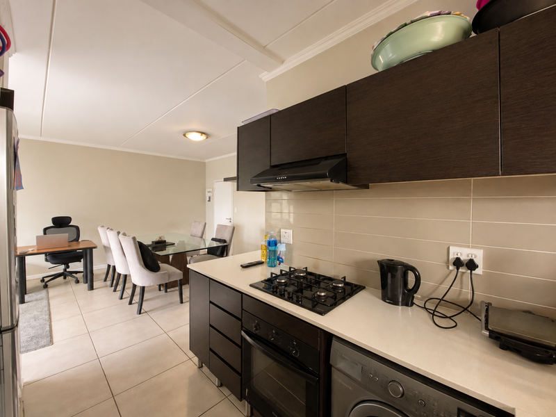 Open-plan kitchen and dining area featuring modern dark cabinetry, stone countertops, gas hob, and tiled flooring throughout the living space.