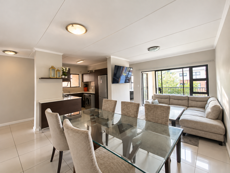Modern open-plan living and dining area featuring tiled floors, a sleek kitchen with built-in cabinetry, and large sliding doors leading to a balcony.