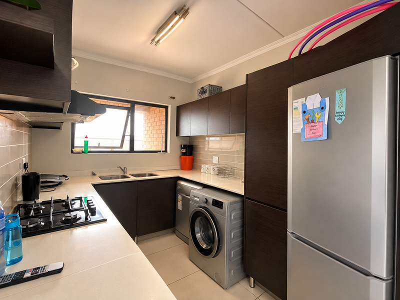 Modern kitchen featuring dark wood cabinetry, stone countertops, a gas hob, extractor fan, and integrated space for laundry appliances.