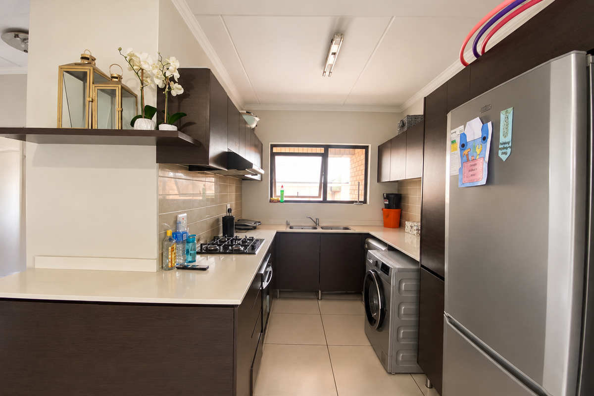A functional kitchen featuring dark wood cabinetry, stone countertops, a gas hob, and integrated laundry space with tiled flooring and backsplash.