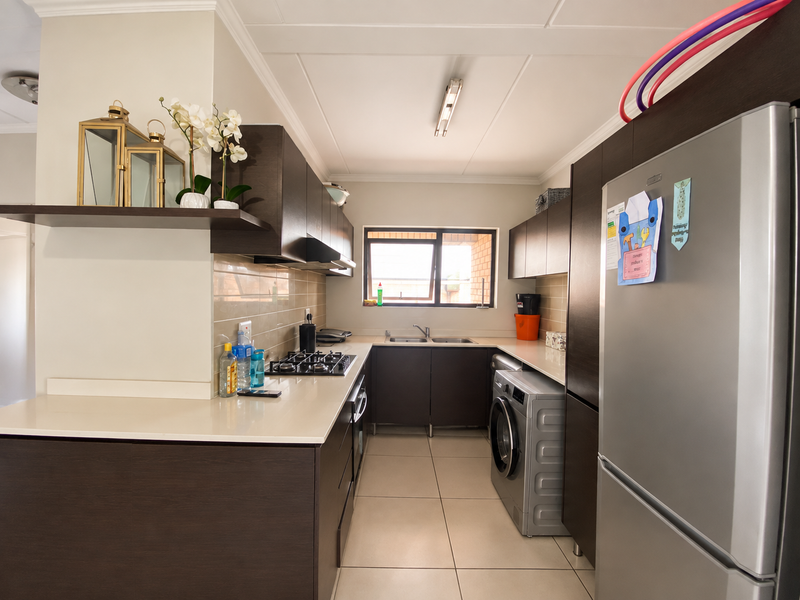A functional kitchen featuring dark wood cabinetry, stone countertops, a gas hob, and integrated laundry space with tiled flooring and backsplash.
