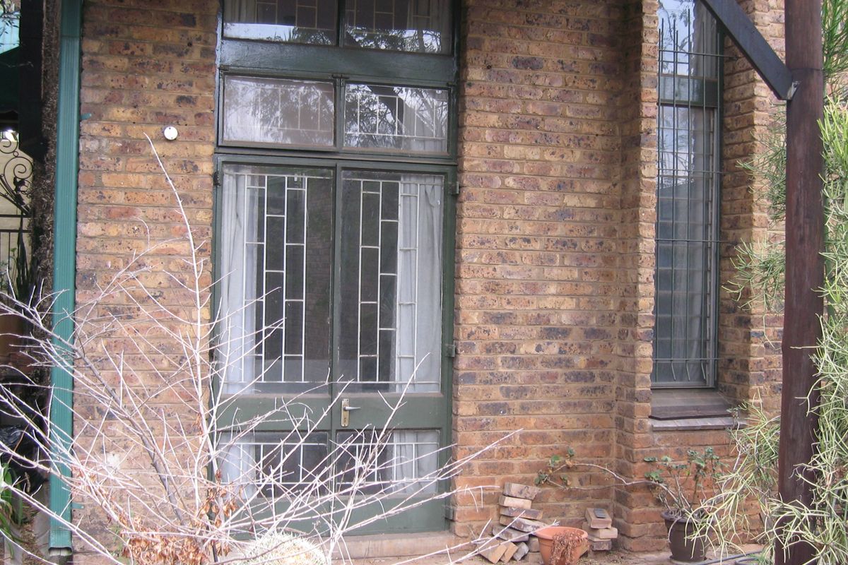 Rear exterior view of a townhouse featuring a face brick facade, security-fitted timber glass doors, and a paved patio area.